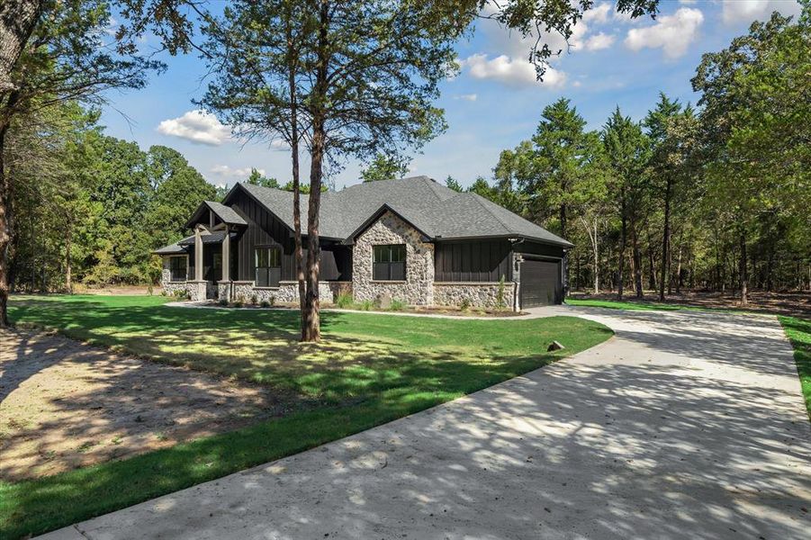 View of front of property with stone siding, board and batten siding, concrete driveway, and a front lawn