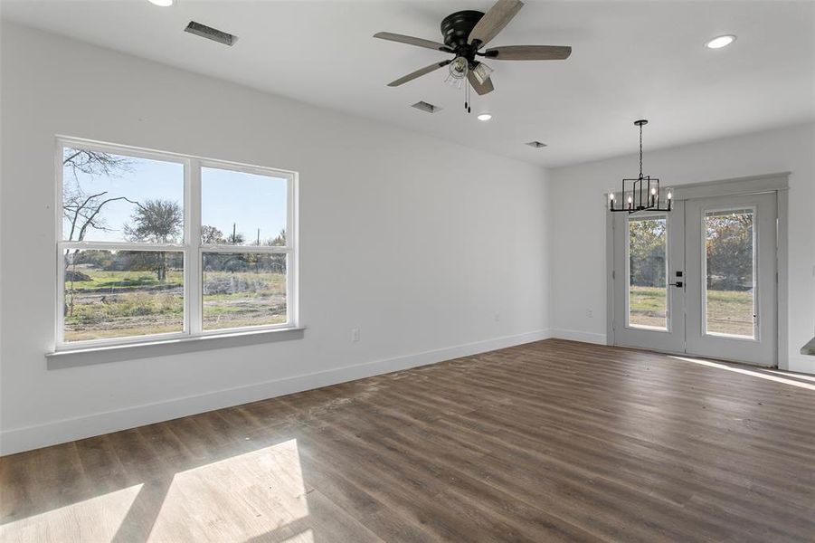 Spare room with dark hardwood / wood-style flooring, plenty of natural light, and ceiling fan with notable chandelier