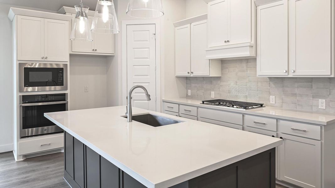 Kitchen featuring appliances with stainless steel finishes, a kitchen island with sink, hanging light fixtures, backsplash, and white cabinetry Kitchen featuring appliances with stainless steel finishes, a kitchen island with sink, hanging light fixtures, backsplash, and white cabinetry