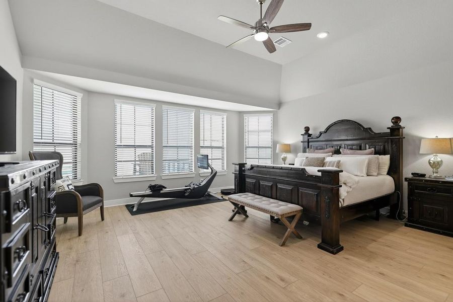 This spacious primary bedroom features a sloped ceiling and ample natural light from bay windows. The room includes a cozy seating area and space for exercise equipment.