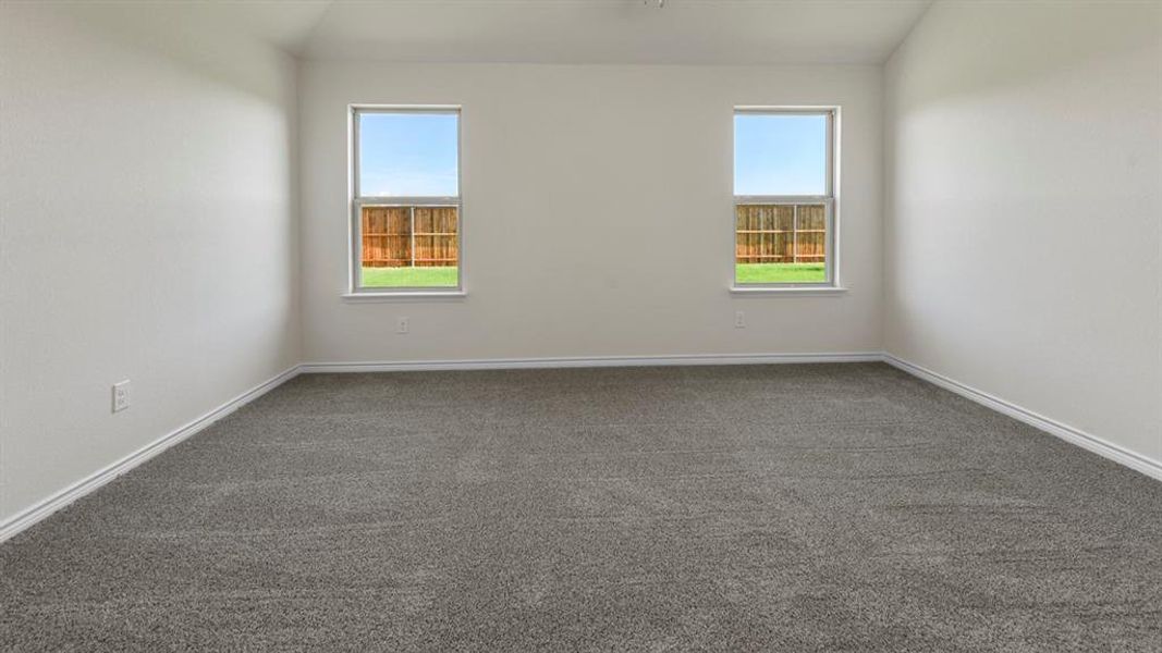 Room featuring two windows providing views of a wooden fence and green lawn, with light-colored walls and grey carpet