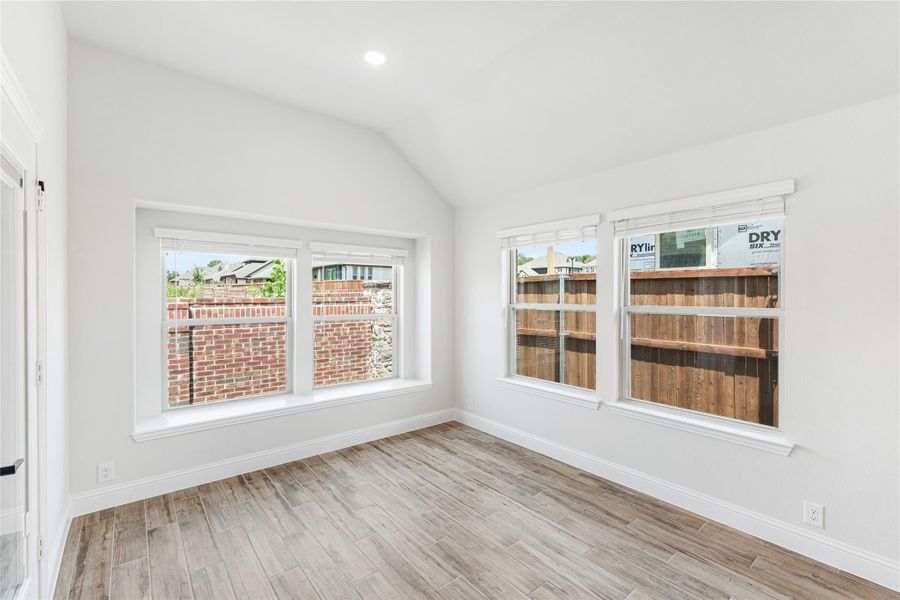 Empty room with vaulted ceiling, wood-look floors, and four windows overlooking a backyard fence