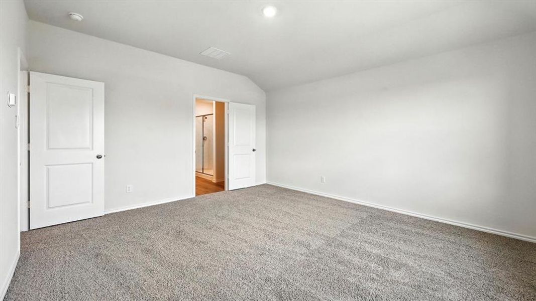 Spacious carpeted room featuring a neutral color palette, multiple paneled doors, and an entryway to a bathroom with a glass-enclosed shower