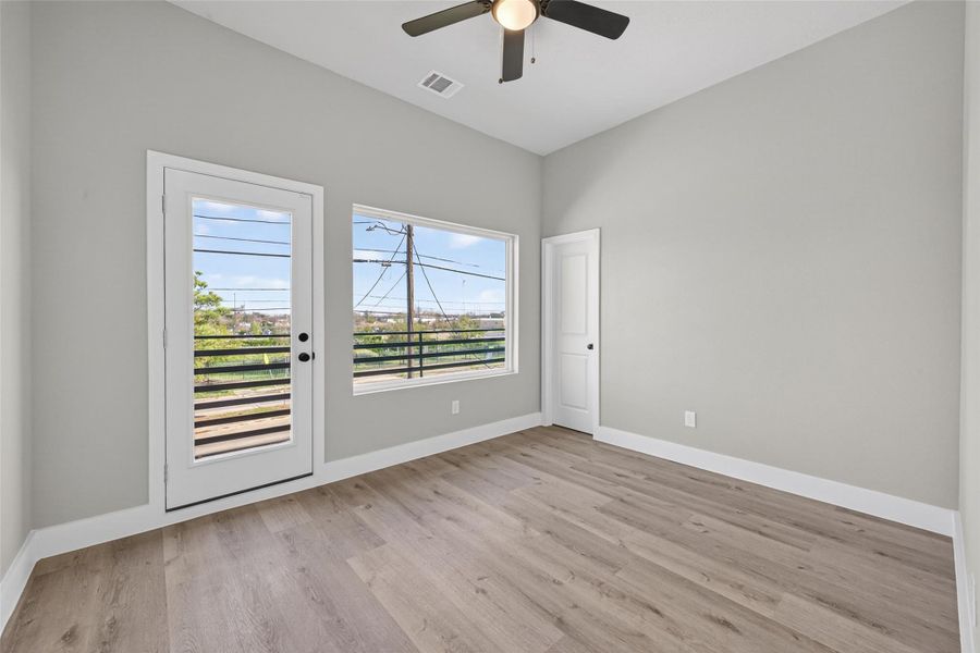 Light-filled secondary bedroom featuring white oak–tone plank laminate flooring, a ceiling fan for year-round comfort, and direct access to a private balcony—ideal for guests or a stylish retreat.