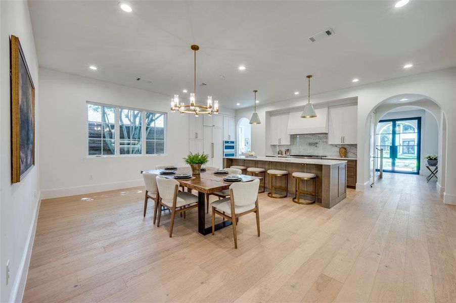 Dining space featuring arched walkways, light wood-type flooring, recessed lighting, and a chandelier