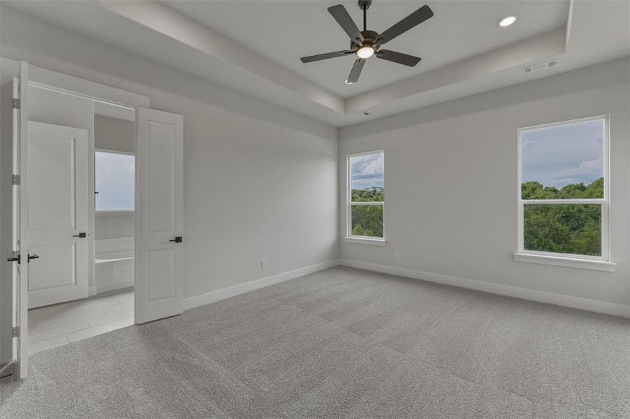 Spacious room featuring light gray carpeting, a tray ceiling with recessed lighting and a ceiling fan, and two large windows Spacious room featuring light gray carpeting, a tray ceiling with recessed lighting and a ceiling fan, and two large windows