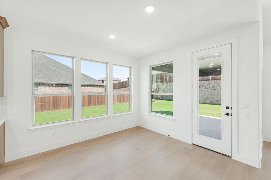 Bright empty room with light wood floors, multiple windows, and a glass back door overlooking a fenced backyard Bright empty room with light wood floors, multiple windows, and a glass back door overlooking a fenced backyard