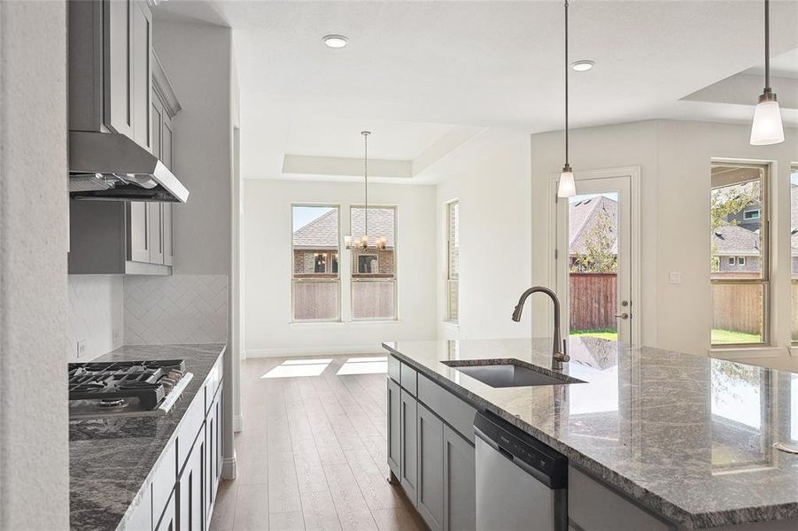 Kitchen with sink, dishwasher, pendant lighting, and dark stone counters