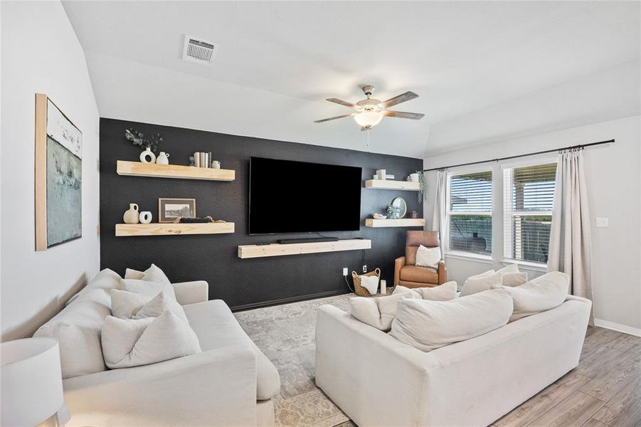 Living area featuring an accent wall, ceiling fan, wood finished floors, and lofted ceiling