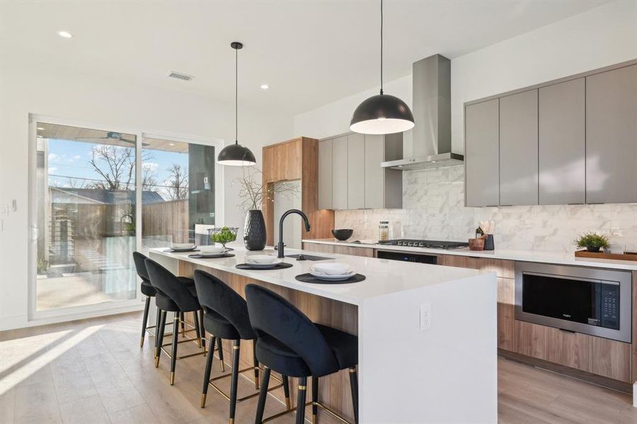 Kitchen featuring tasteful backsplash, ventilation hood, hanging light fixtures, black microwave, and gray cabinets