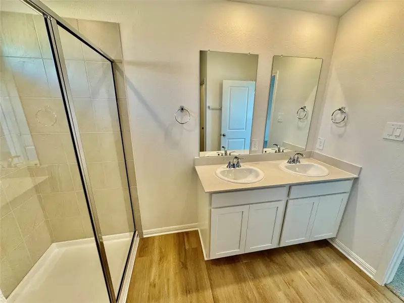 Full bath with a textured wall, a stall shower, light wood-type flooring, and double vanity