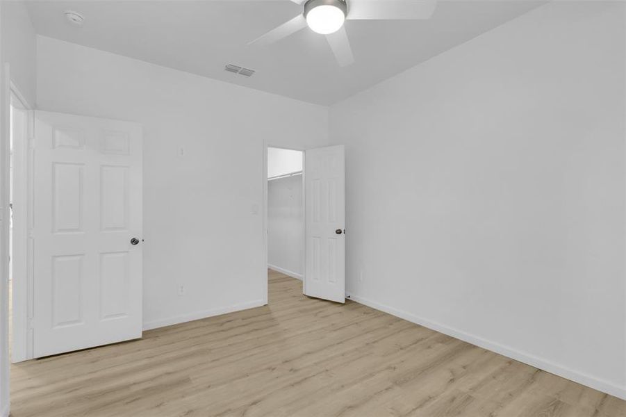 Unfurnished bedroom with light wood-type flooring, a spacious closet, and a ceiling fan