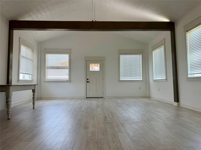 A spacious room features a light wood-look floor, an entry door, and numerous windows.