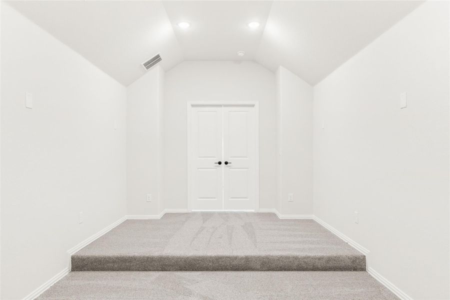 Empty room with vaulted ceiling, gray carpet, and white double doors at the end Empty room with vaulted ceiling, gray carpet, and white double doors at the end
