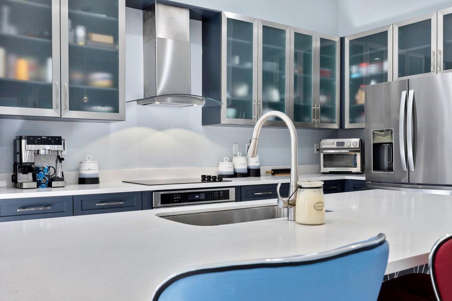 Kitchen with wall chimney range hood, stainless steel refrigerator with ice dispenser, glass insert cabinets, and light stone countertops