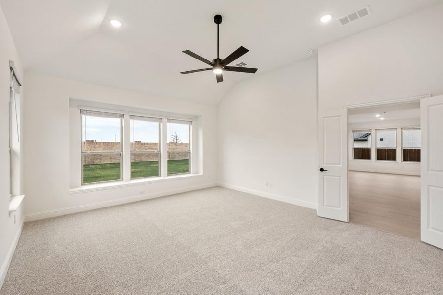 Empty bedroom with vaulted ceiling, ceiling fan, carpet flooring, and large window overlooking backyard Empty bedroom with vaulted ceiling, ceiling fan, carpet flooring, and large window overlooking backyard