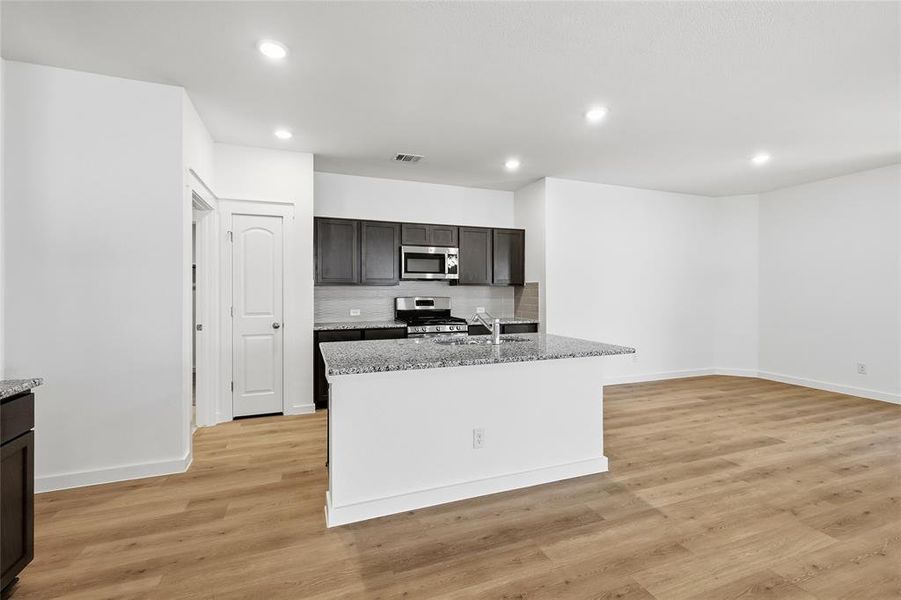 Kitchen with light stone counters, a kitchen island with sink, stainless steel appliances, light wood-style floors, and recessed lighting