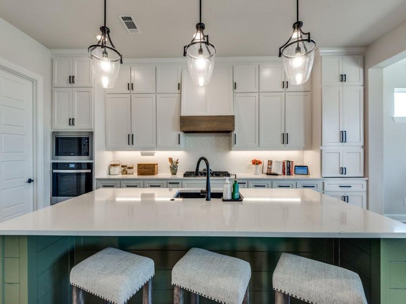 Kitchen featuring white cabinetry, oven, decorative light fixtures, and a kitchen island with sink