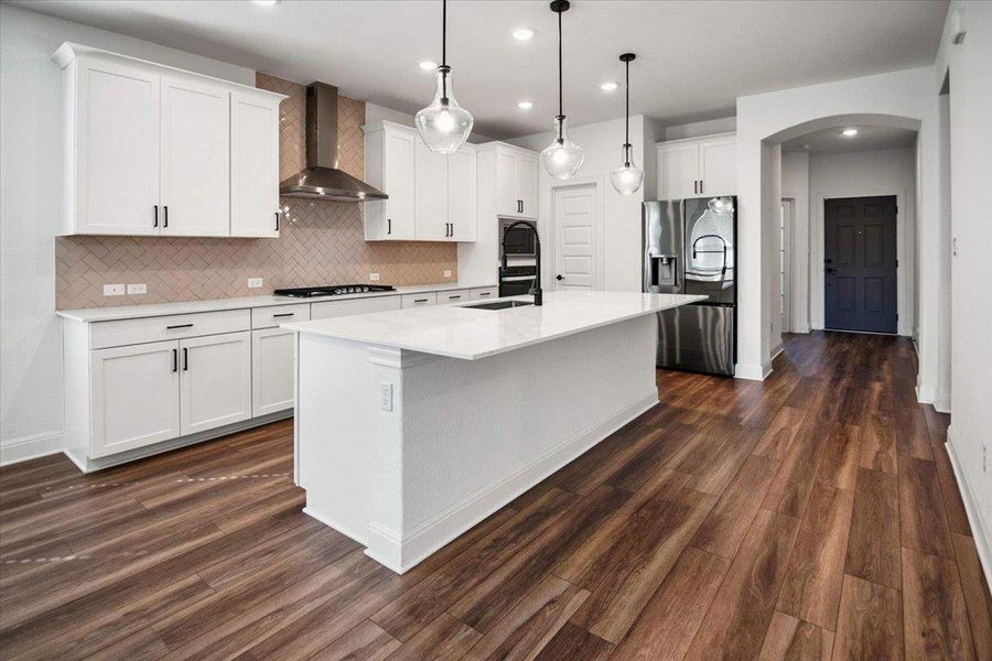 A well-appointed kitchen features a large central island, overhead pendant lighting, and a stainless steel range hood.