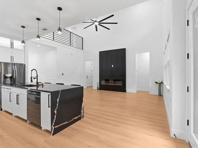 Open-concept living space featuring high ceilings, wood-finish flooring, and a modern kitchen island with a waterfall countertop