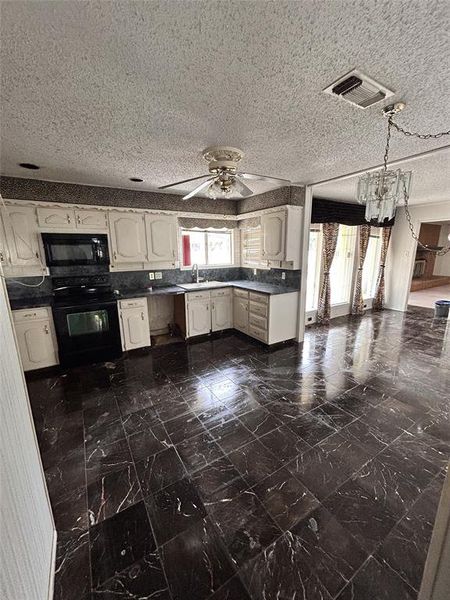 Kitchen with black appliances, healthy amount of natural light, dark marble finish flooring, a textured ceiling, and dark countertops Kitchen with black appliances, healthy amount of natural light, dark marble finish flooring, a textured ceiling, and dark countertops