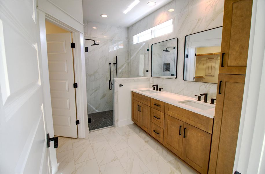 Bathroom featuring light marble finish floors, double vanity, and a marble finish shower