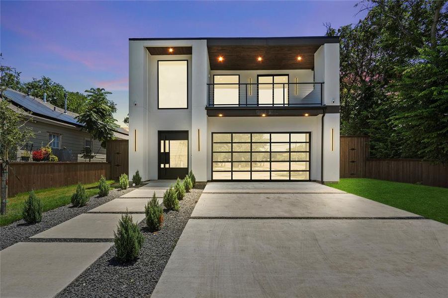 Contemporary home featuring a balcony, concrete driveway, a garage, and stucco siding
