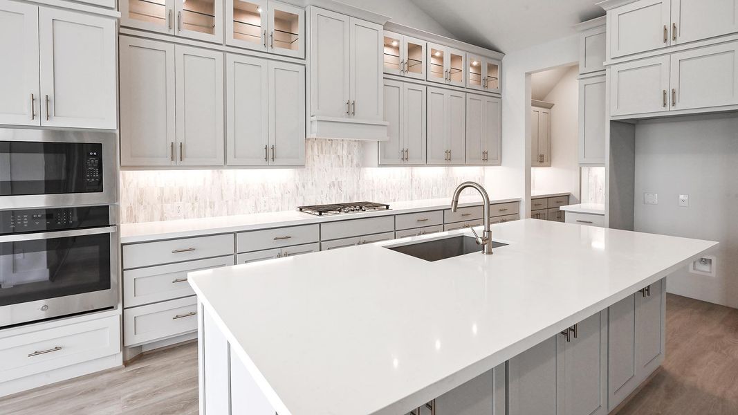Kitchen with appliances with stainless steel finishes, vaulted ceiling, light wood-style flooring, tasteful backsplash, and an island with sink