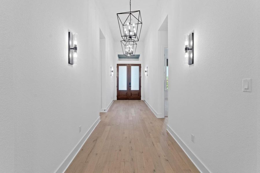 Corridor with light wood-type flooring, a textured wall, and a chandelier Corridor with light wood-type flooring, a textured wall, and a chandelier