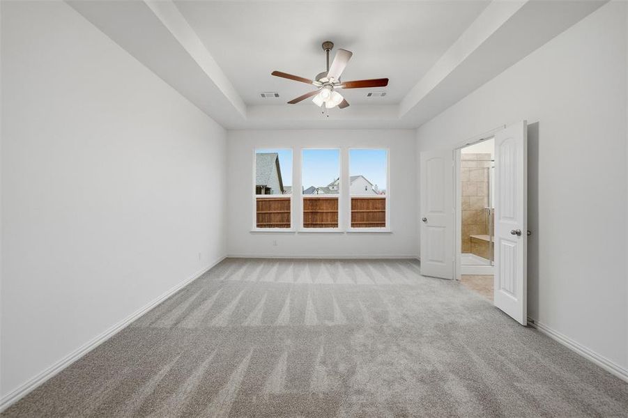Empty room featuring ceiling fan, light colored carpet, and a raised ceiling