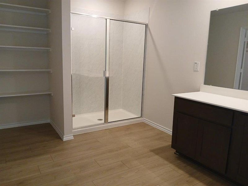 Bathroom featuring a glass-enclosed shower, wood-finish flooring, built-in shelving, a dark wood-finish vanity with a light-toned countertop, and a wall-mounted mirror Bathroom featuring a glass-enclosed shower, wood-finish flooring, built-in shelving, a dark wood-finish vanity with a light-toned countertop, and a wall-mounted mirror