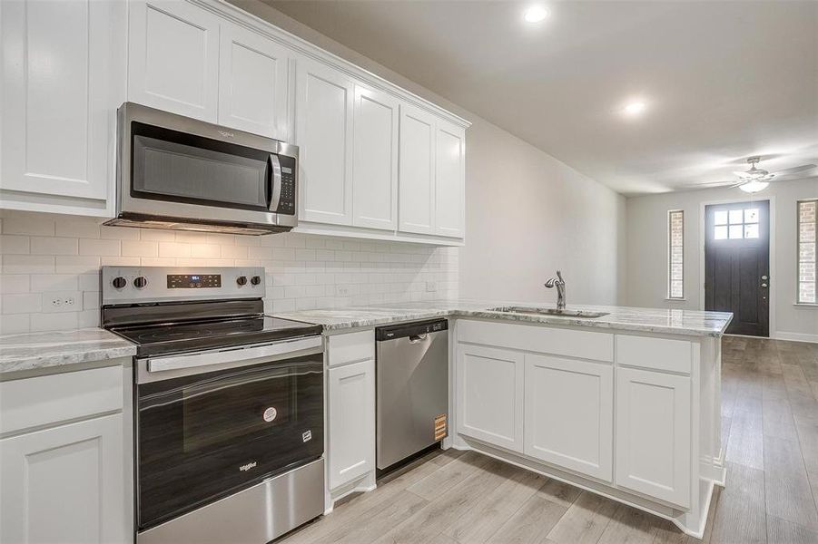 Kitchen featuring stainless steel appliances, a peninsula, light stone counters, white cabinets, and recessed lighting