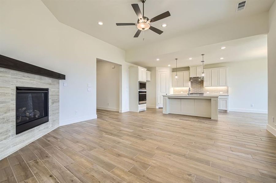 Unfurnished living room featuring a tile fireplace, baseboards, visible vents, and light wood-type flooring