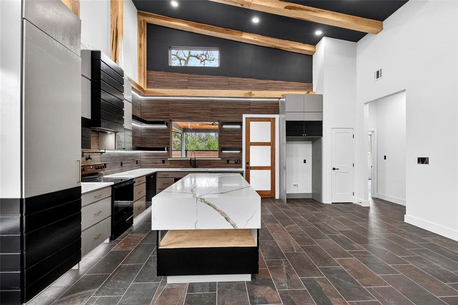 Two tone kitchen with a center island, modern cabinets, light stone countertops, black / electric stove, and vaulted ceiling