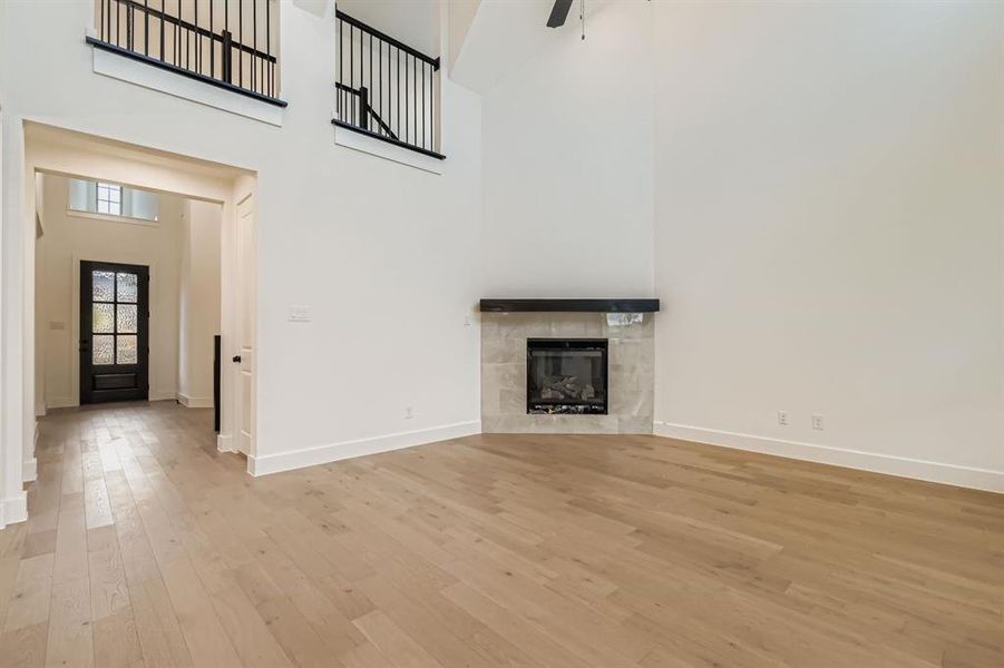 Unfurnished living room with a towering ceiling, a fireplace, light wood-style floors, and ceiling fan Unfurnished living room with a towering ceiling, a fireplace, light wood-style floors, and ceiling fan