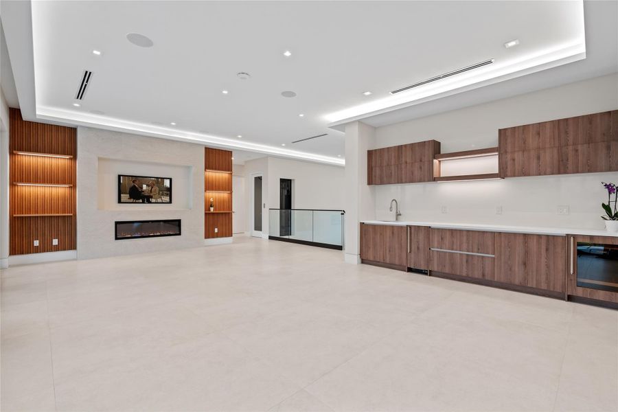 Spacious upstairs living area with sleek built-in wet bar, modern fireplace, and custom wood accents creating the perfect entertainment retreat. Spacious upstairs living area with sleek built-in wet bar, modern fireplace, and custom wood accents creating the perfect entertainment retreat.
