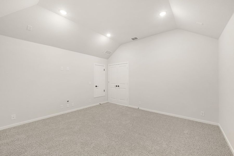 Empty bedroom with vaulted ceiling, recessed lighting, gray carpet, and two white doors