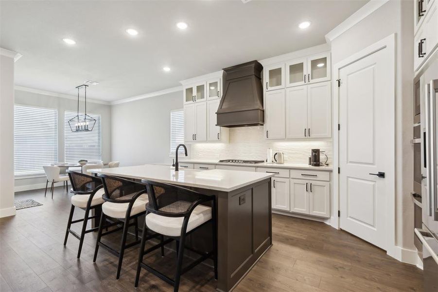 Kitchen featuring white cabinets, custom range hood, a kitchen island with sink, and hanging light fixtures