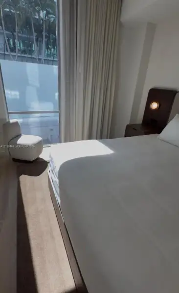 Floor-to-ceiling windows, wood-finish flooring, and built-in dark wood headboard featuring integrated circular wall-mounted lighting