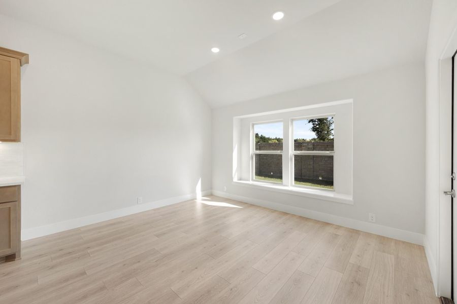 Empty room with vaulted ceiling, light wood floors, and a large double window with natural light Empty room with vaulted ceiling, light wood floors, and a large double window with natural light