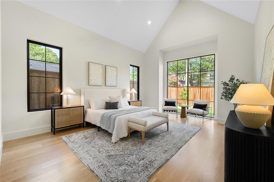 Vaulted ceilings accent this room featuring large black-framed windows, light wood-finish flooring, and white walls
