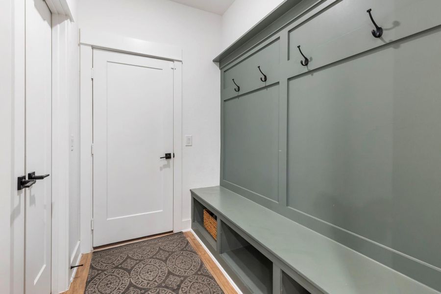 This mudroom features a built-in bench with storage cubbies and multiple wall hooks, perfect for organizing coats and shoes. The space is bright with white walls and a decorative rug, providing a functional entryway.