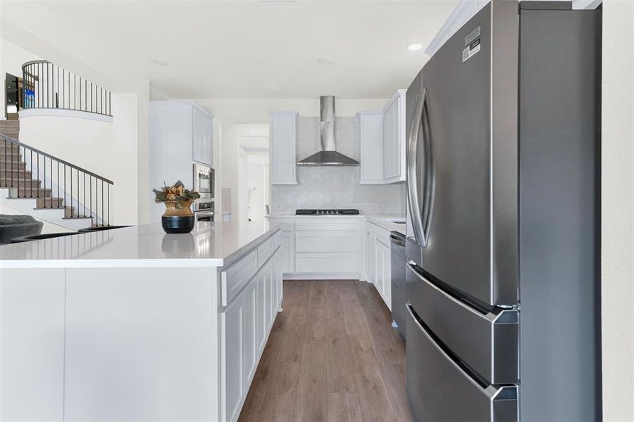 Kitchen featuring appliances with stainless steel finishes, tasteful backsplash, light wood-type flooring, wall chimney exhaust hood, and white cabinetry Kitchen featuring appliances with stainless steel finishes, tasteful backsplash, light wood-type flooring, wall chimney exhaust hood, and white cabinetry