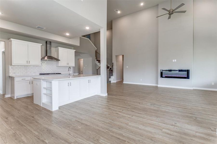 Kitchen featuring white cabinetry, a towering ceiling, light hardwood / wood-style floors, and wall chimney range hood