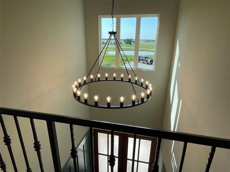 Grand entryway featuring a large circular chandelier with exposed bulbs, an ornate black metal staircase railing, and a window with a rural landscape