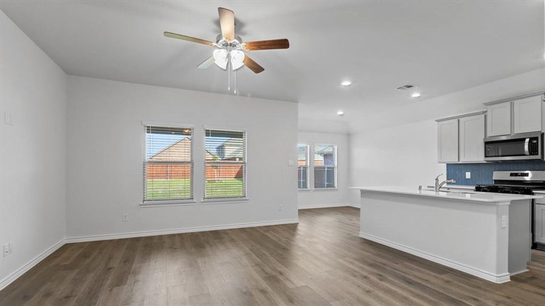 Kitchen with backsplash, stainless steel appliances, a ceiling fan, a center island with sink, and dark wood finished floors