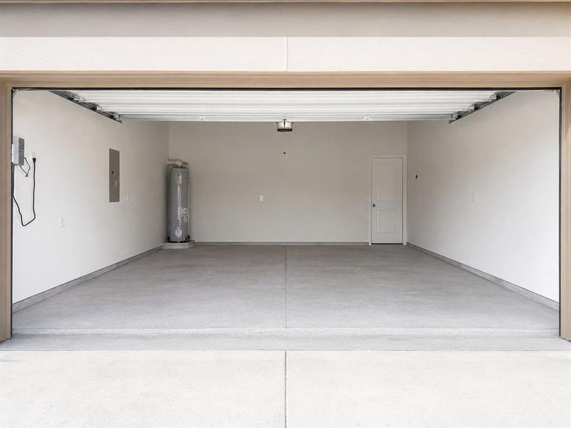Spacious garage featuring concrete flooring, a water heater, and a side access door