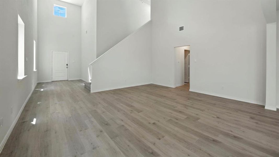 Unfurnished living room featuring a towering ceiling, stairs, and light wood finished floors