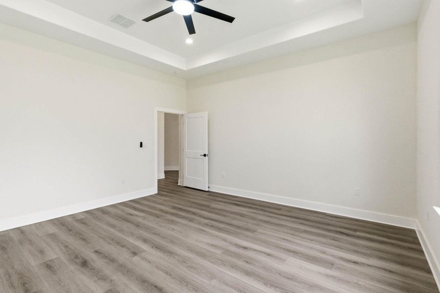 A pristine bedroom features light wood flooring and a recessed ceiling with a modern fan. A pristine bedroom features light wood flooring and a recessed ceiling with a modern fan.