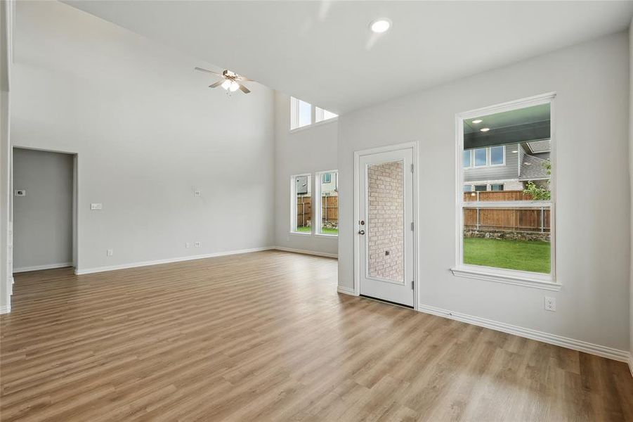 Unfurnished living room featuring a ceiling fan, light wood-style floors, baseboards, and a towering ceiling Unfurnished living room featuring a ceiling fan, light wood-style floors, baseboards, and a towering ceiling